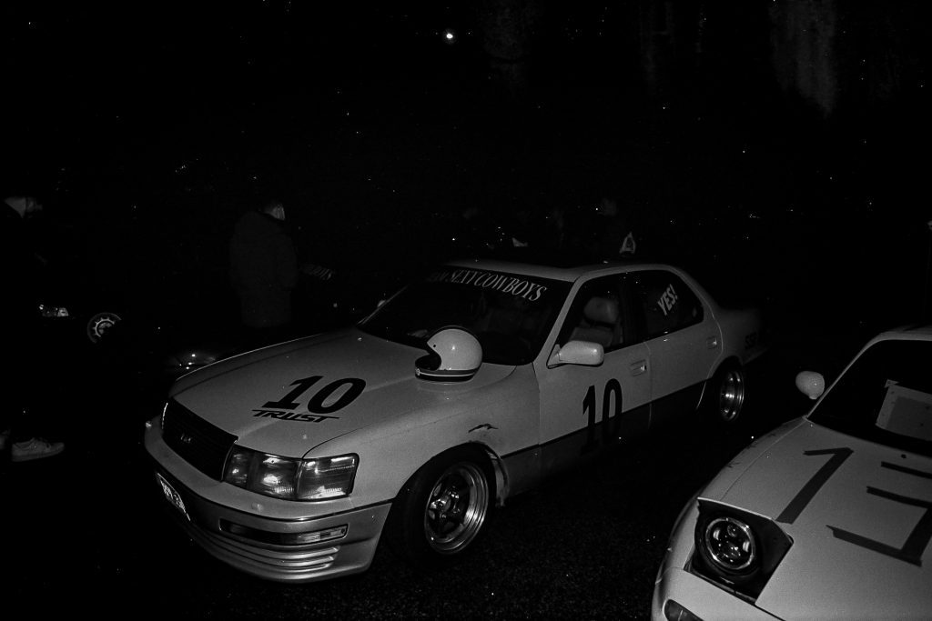 Black and white photo of a race car with Monkey Cowboys and Trust decals, and the number 10 at night.