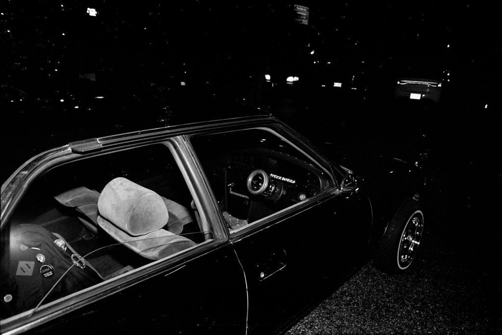 Black and white photo of a parked car at night, showing interior details with a Japanese sticker reading 走行戦士 (Race Warrior).
