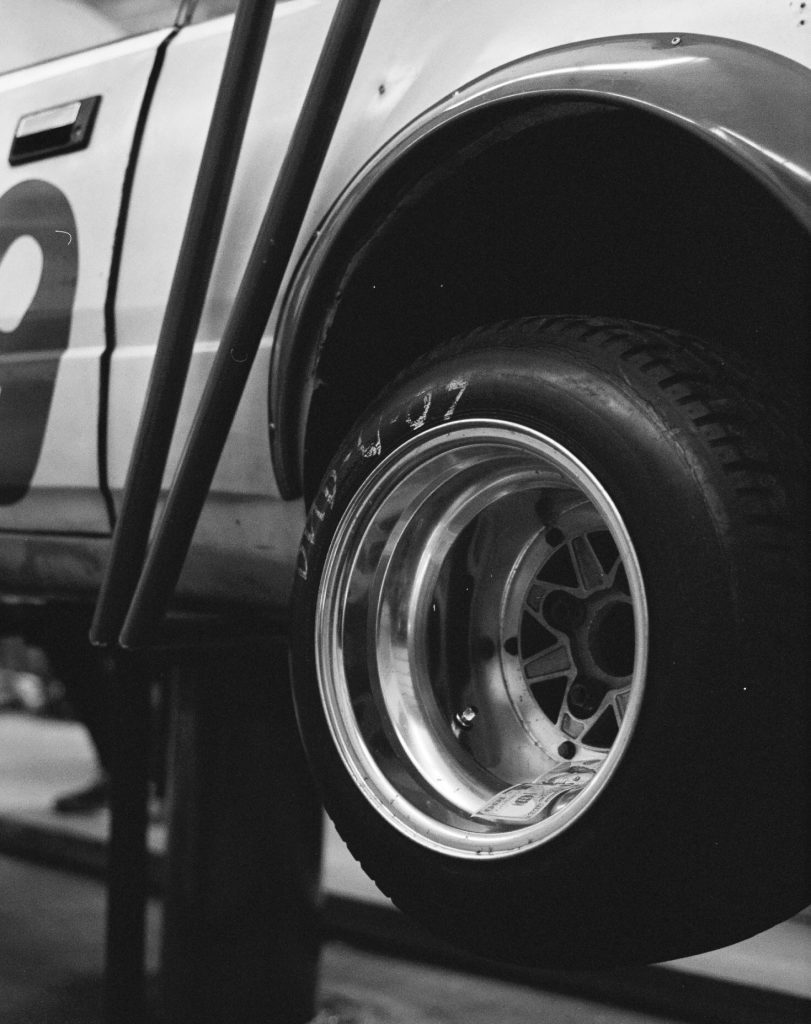 Black and white photo of a vintage race car's rear tire and wheel, featuring the number 0 on the vehicle's side.