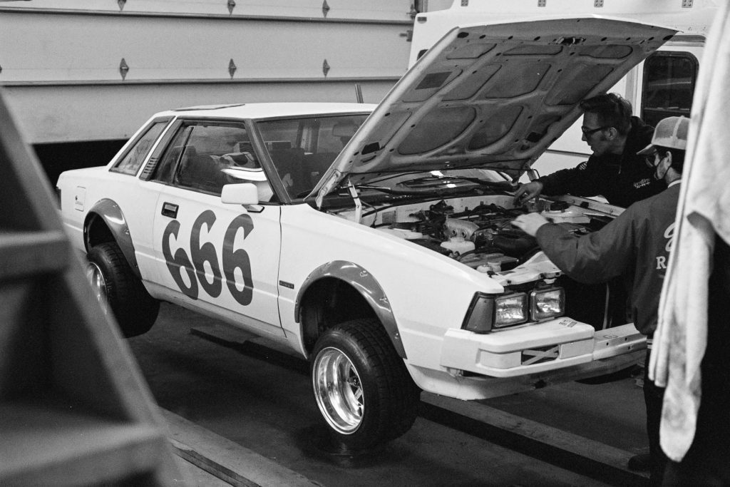 Mechanics working under the hood of a white race car with number 666 in a garage.