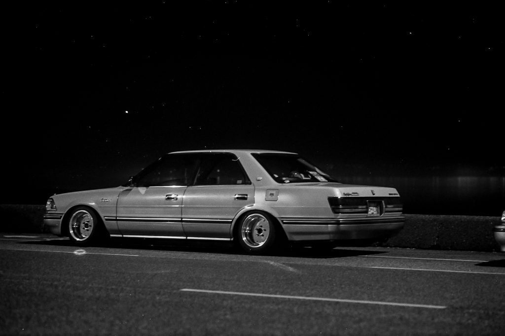 Vintage Japanese sedan car parked at night by the road with a clear view of the starry sky.
