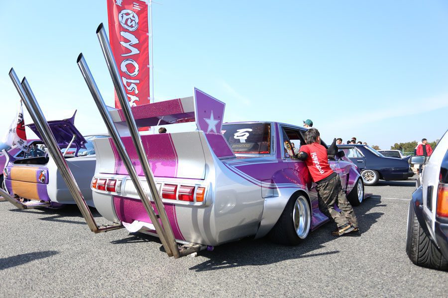 Custom purple and silver bosozoku-styled cars with exaggerated exhausts and body kits at a Japanese car event.