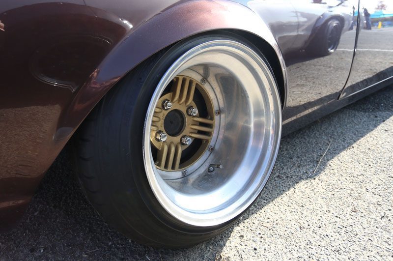 Close-up of a bronze deep-dish alloy wheel on a lowered car with stretched tires, showcasing a sleek custom modification.