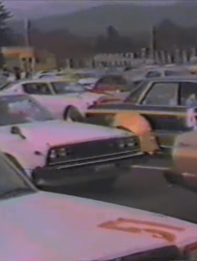 A video still of cars entering a race track in the 1970s