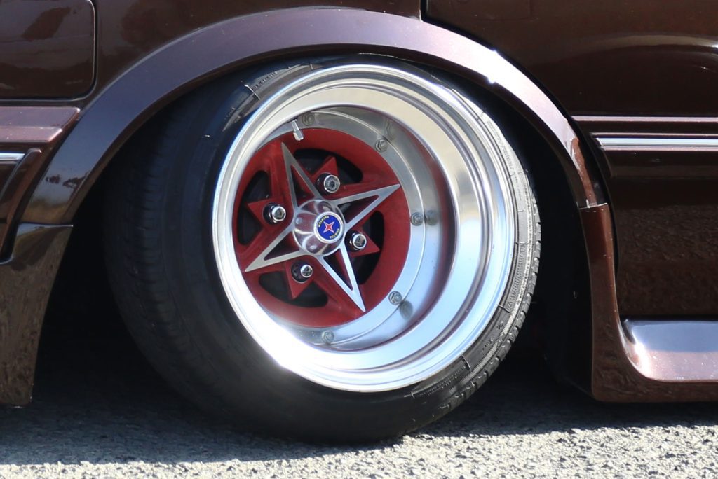 Close-up of a red and silver star-shaped alloy wheel on a brown car, with visible tire details.