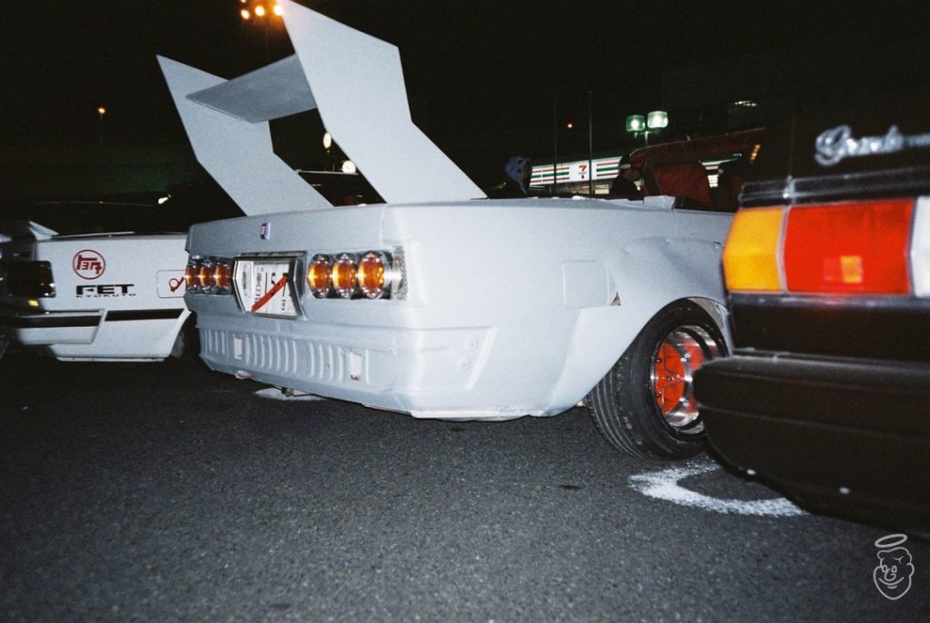 Modified vintage Japanese car with large spoiler and FET logo, at a nighttime car meet.