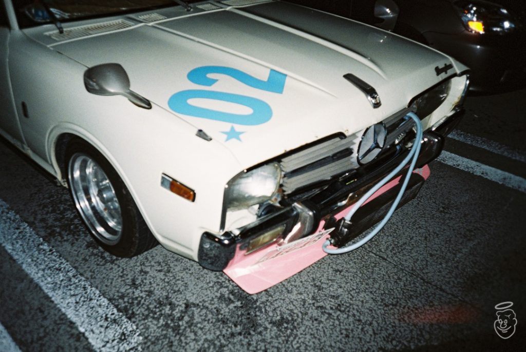 Vintage white car with blue '02' number and star on the hood, retrofitted for racing, parked on a street.