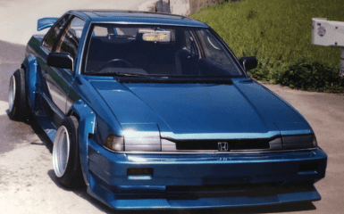 Modified blue Honda with wide body kit and TRUST sticker on windshield parked on a road.