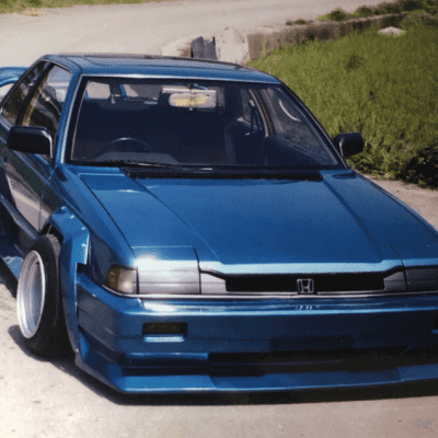 Modified blue Honda with wide body kit and TRUST sticker on windshield parked on a road.