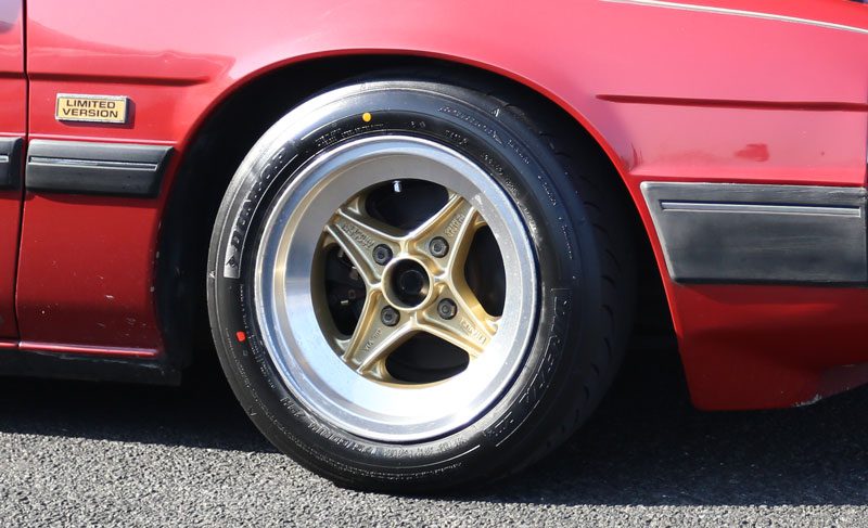 Close-up of a red limited edition car with shiny gold alloy wheel on a black tire, parked on a pavement.