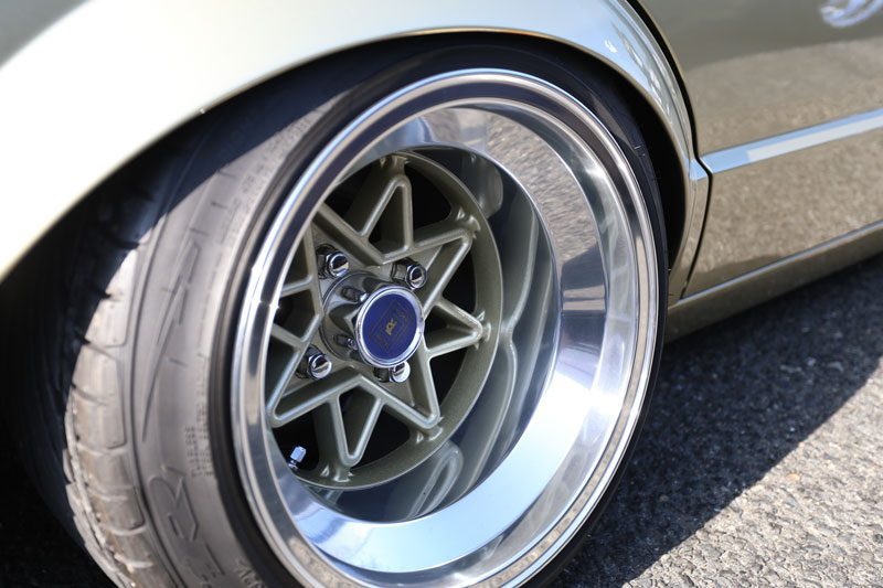 Close-up of a custom alloy car wheel with RS logo, matte green spokes, and polished lip on asphalt background.