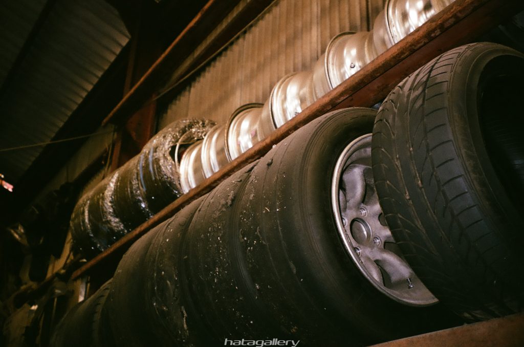 Stacked used car tires and wheel rims in a dimly lit garage, showing signs of wear, with hatogallery watermark.
