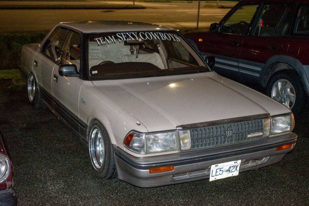 Modified Toyota Crown in a parking lot, with TEAM SEXY COWBOYS decal on the windshield, at night.