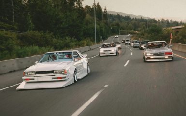 A convoy of modified JDM cars with R.B.S decals on a highway, surrounded by lush greenery, showcasing car culture.