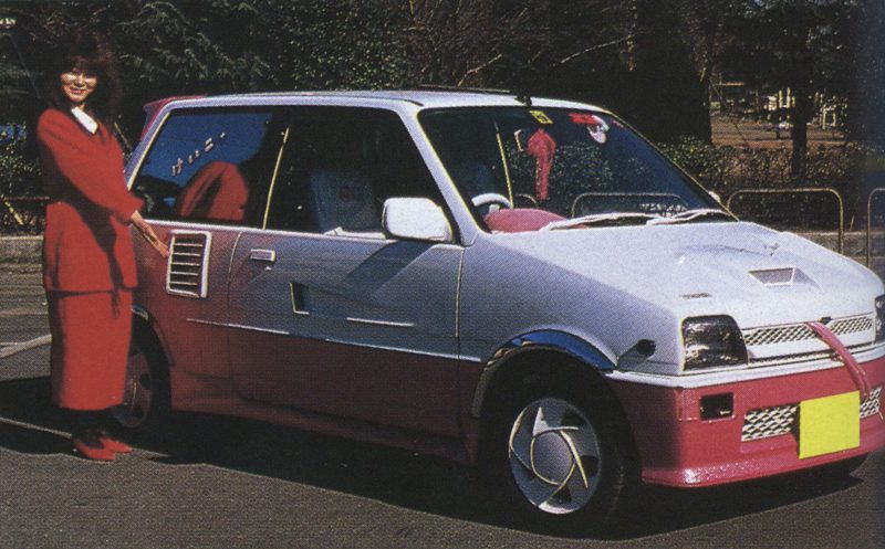 Woman posing with a customized k-car featuring a pink and white two-tone paint job, with Japanese text あきら on window.