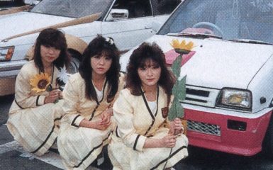 Three women in uniforms holding flowers in front of decorated cars in a Japanese car show. レディース on car windshield.Explanation:
The alt text describes the main elements in the image including the women, their uniforms, the flowers they are holding, and the Japanese car show setting to ensure it is relevant and improves SEO.