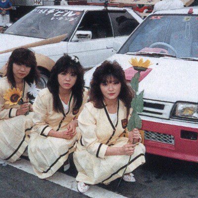 Three women in uniforms holding flowers in front of decorated cars in a Japanese car show. レディース on car windshield.Explanation:
The alt text describes the main elements in the image including the women, their uniforms, the flowers they are holding, and the Japanese car show setting to ensure it is relevant and improves SEO.