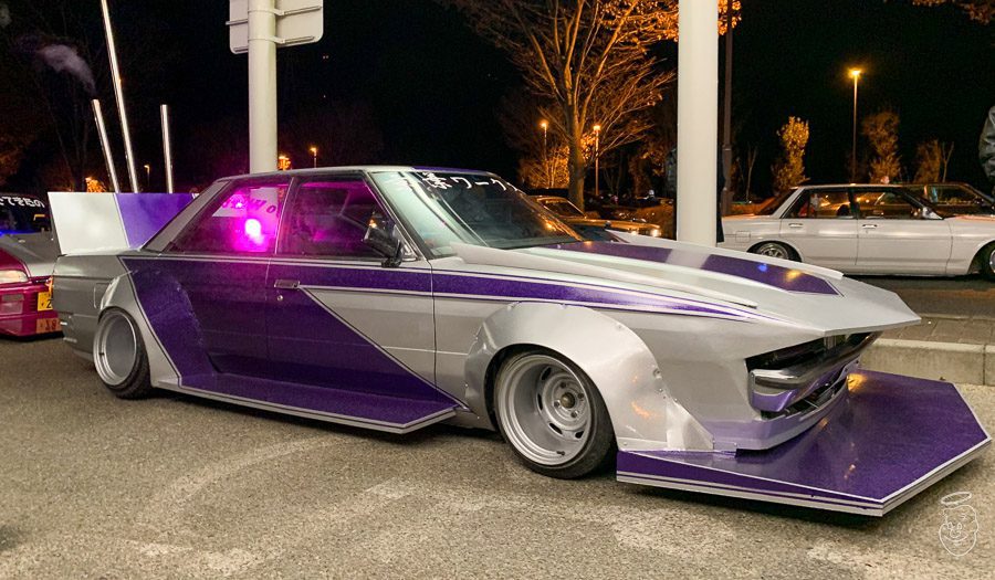 Custom Japanese car with purple and silver paint, featured at a night car show. Text on windshield is in Japanese.