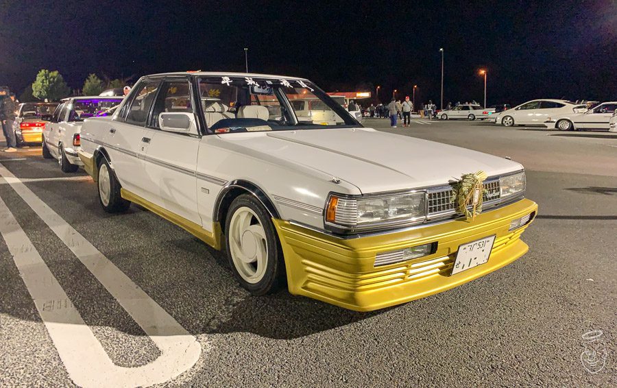 Modified vintage white and gold car with a Japanese number plate at a night car meet.