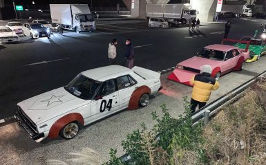 Vintage Japanese modified cars parked under an overpass at night with people standing nearby.