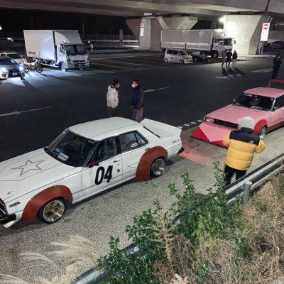 Vintage Japanese modified cars parked under an overpass at night with people standing nearby.