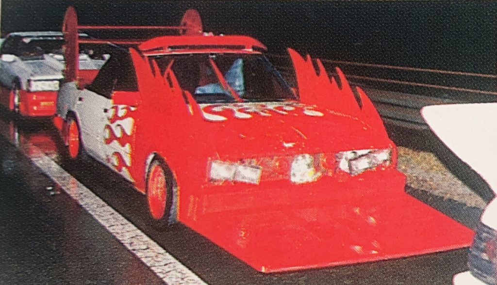 Custom Japanese Bosozoku car with red flames and oversized front splitter parked on the road at night.