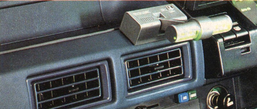 Close-up of car dashboard featuring dual air vents, climate control buttons, and a device mounted above the vents.