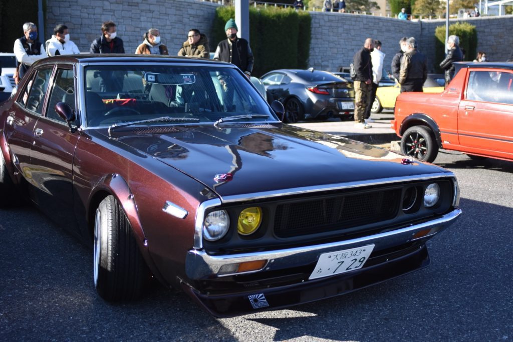 Vintage Japanese car at a car meet, Osaka license plate number 7 29, with people gathered in the background.