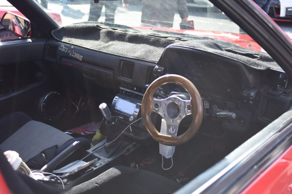 Interior of a classic Japanese sports car featuring a wooden steering wheel and Hiro Motor logo on the dashboard.