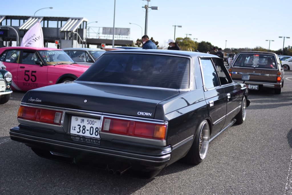 Vintage Japanese cars showcased at an automotive event, including a modified Toyota Crown by Super Saloon and a pink racer with Route 55.