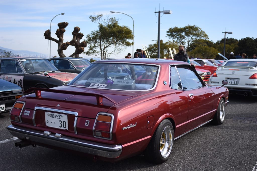 Vintage Japanese cars showcased at an outdoor car meet, featuring a maroon classic model with chrome detailing.