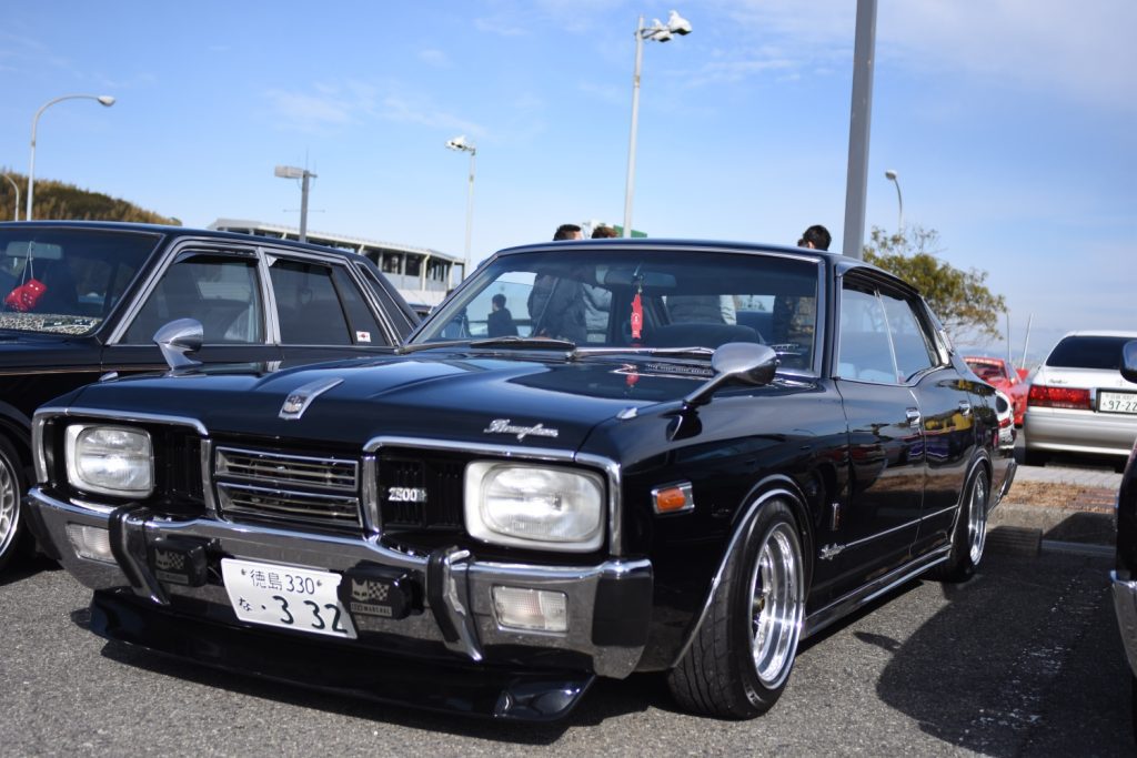 Classic black Nissan sedan parked at a car show, vintage Japanese car with chrome details under a clear blue sky.