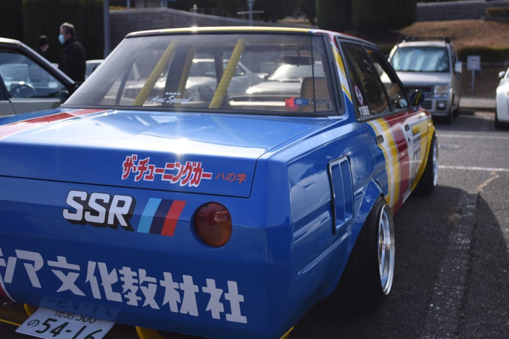 Close-up of a colorful modified car with SSR logo, Japanese text The Tuning Car, and roll cage at an automotive event.