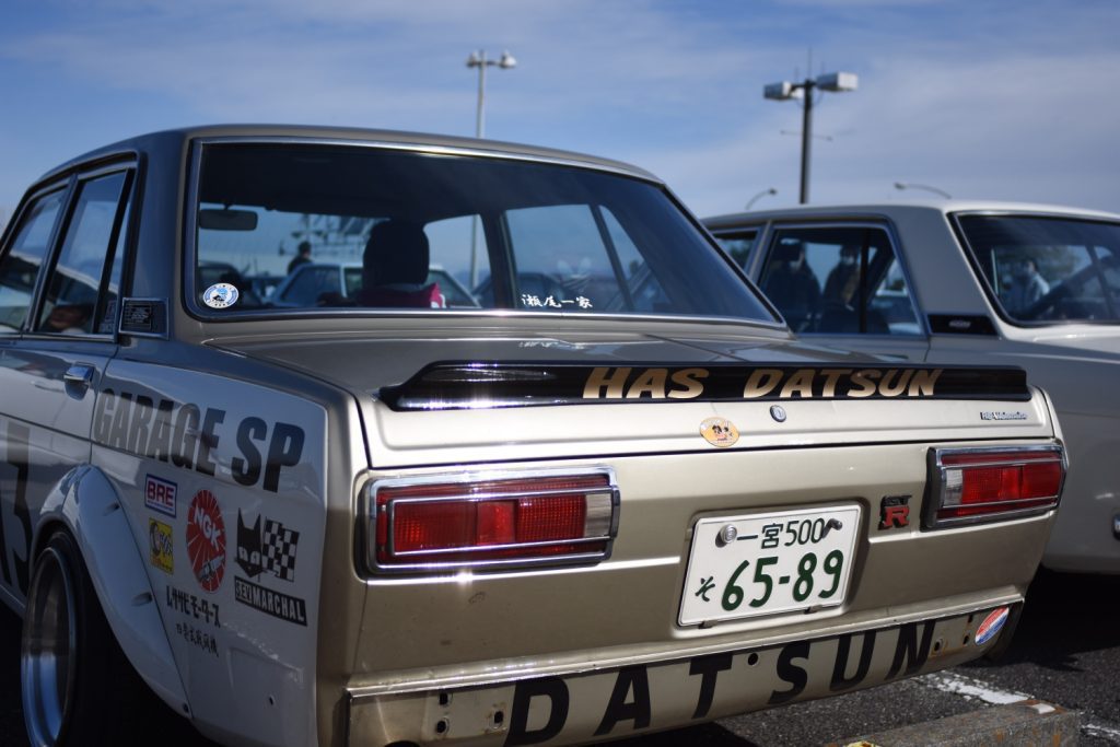 Vintage Datsun car with GARAGE SP and HAS DATSUN stickers, Japanese license plate 65-89, and race decals.