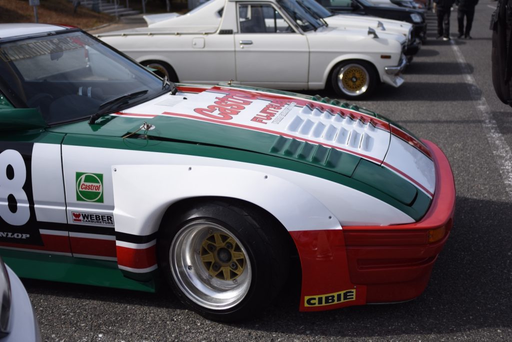 Vintage car event featuring a green, red, and white racing car with Castrol logos and retro cars in the background.