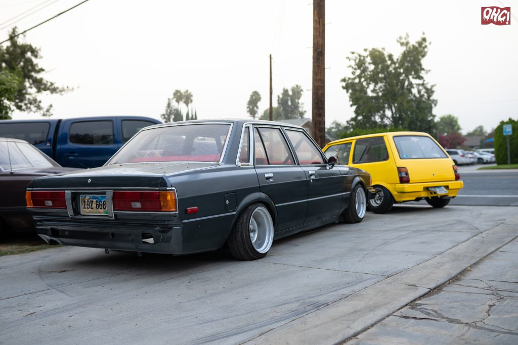 Two cars parked on a concrete driveway: a gray sedan and a yellow hatchback with lowered suspension.