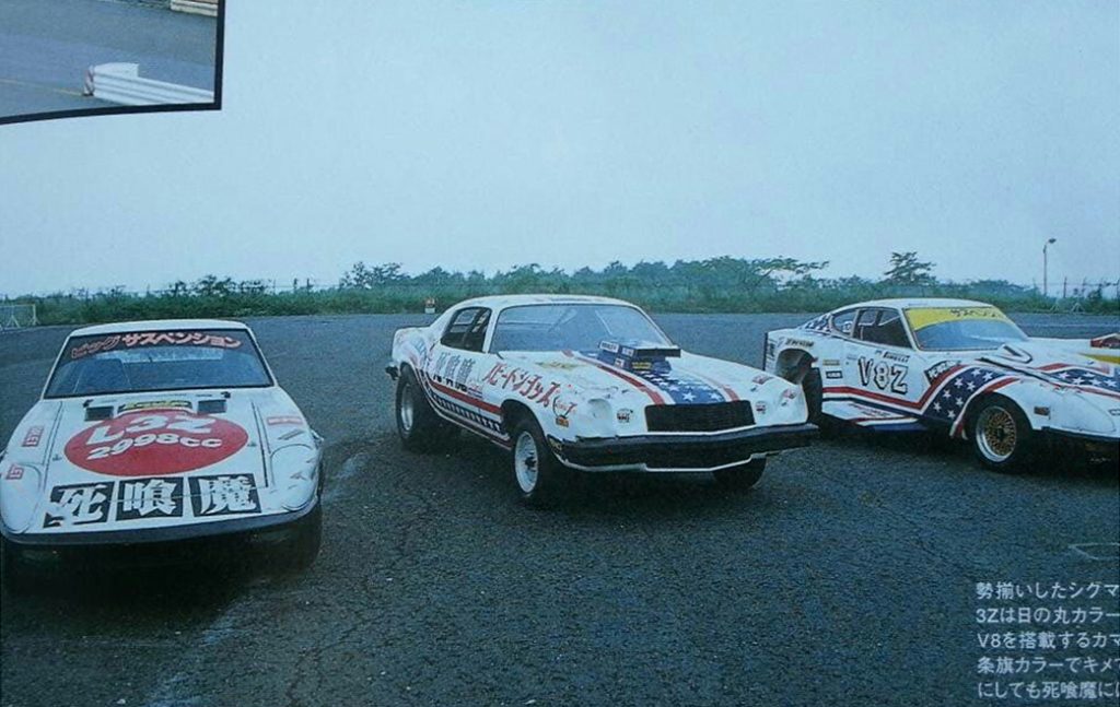 Three modified sports cars with Japanese text decals, racing graphics, and American themes parked on asphalt.