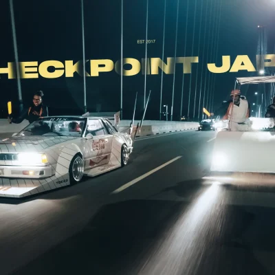 Vintage cars on a Japanese bridge at night with the text Checkpoint Japan.