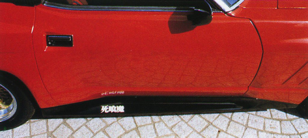 Red sports car side view with Japanese 死亡遊戯 text, translated Game of Death, on black side skirt.