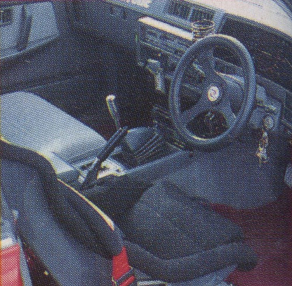 Interior of a vintage car with a racing seat, manual transmission, and a three-spoke steering wheel with Japanese kanji.