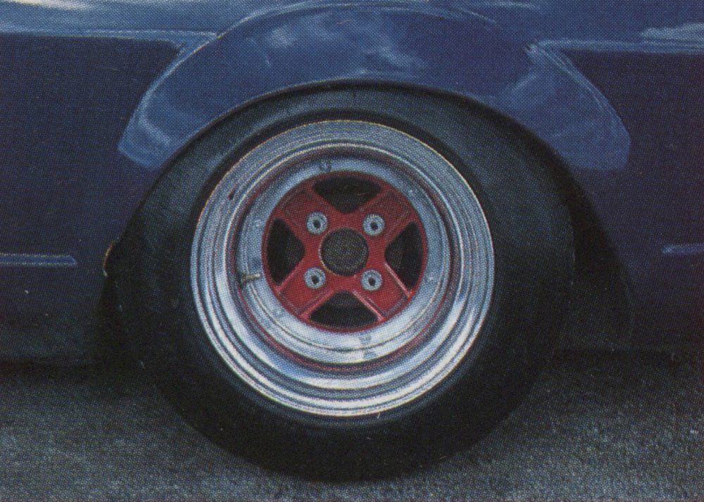 Close-up of a classic car's chrome wheel with a red hub, parked on a gray surface.