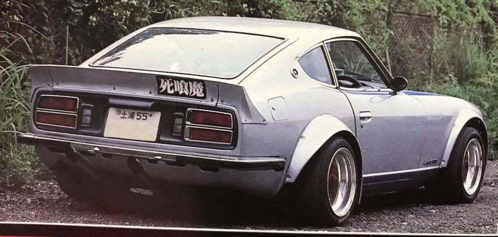 Rear view of a modified vintage Japanese car with deep-dish wheels and a spoiler. Japanese text reads death demon.