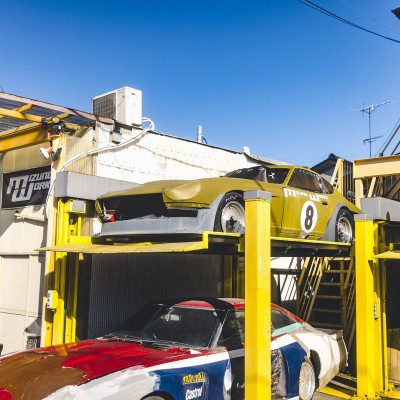 Vintage racing cars at Izumo Works garage in Japan on a sunny day. The sign reads Izumo Works (イズモワークス).