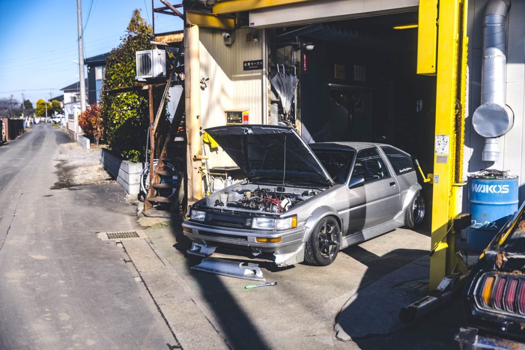Silver modified car with an open hood being repaired in a garage in Japan, sign reads Kitayama Works (北山ワークス).