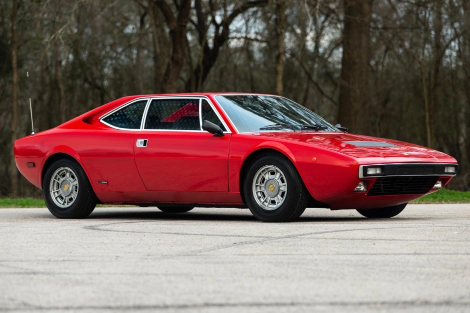 Red classic sports car parked outdoors with trees in the background, showcasing a sleek design and vintage aesthetic.
