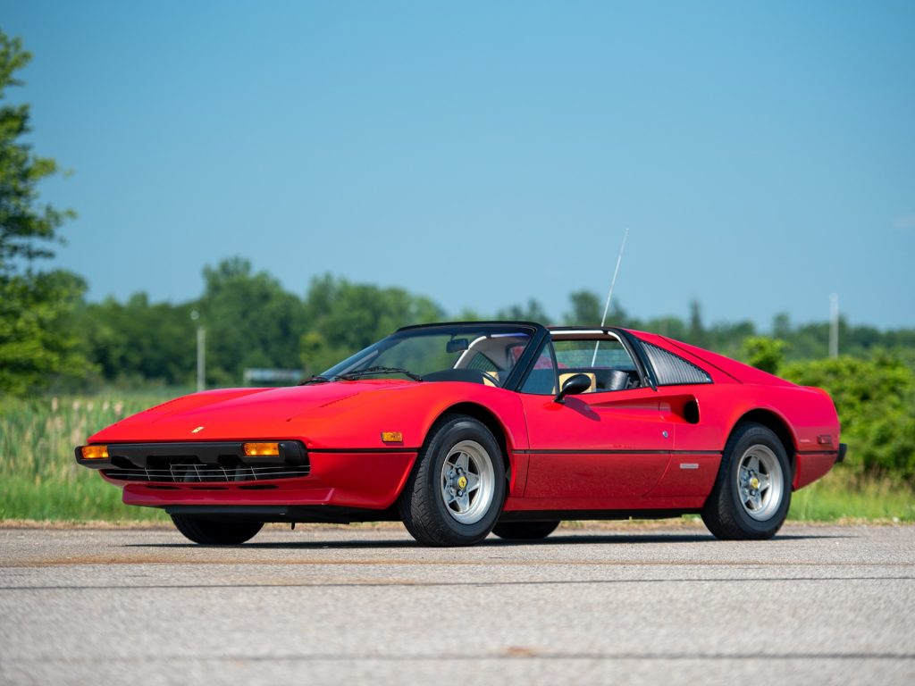 Red classic sports car parked outdoors on a clear sunny day with green landscape in the background.