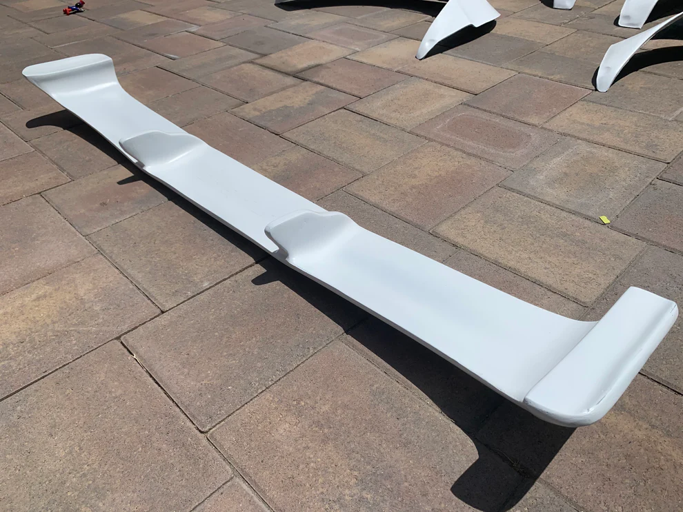 White car spoiler on a tiled ground, likely for enhancing aerodynamic performance of a vehicle.