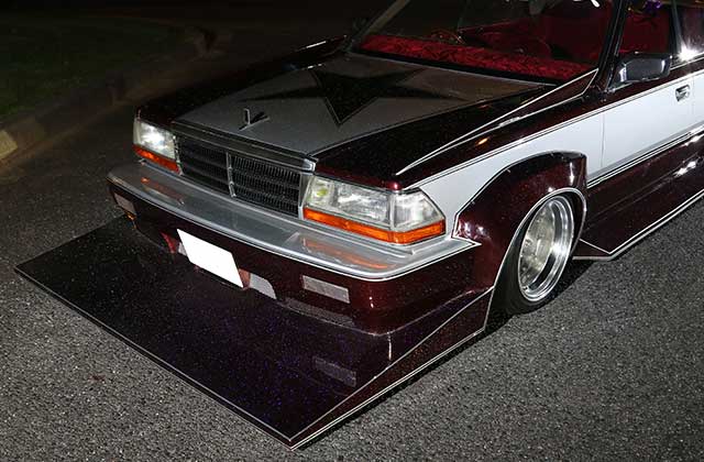 Customized retro Japanese car with a large front splitter, shining under streetlights on a smooth asphalt road at night.