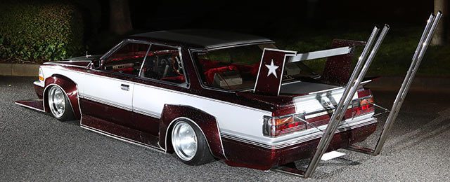 Heavily modified Japanese car with large exhaust pipes, custom spoiler, and star design. Bosozoku style at night.