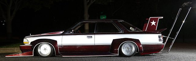 Modified Japanese car with a large spoiler and custom body kit in a Bosozoku style, parked on a street at night.
